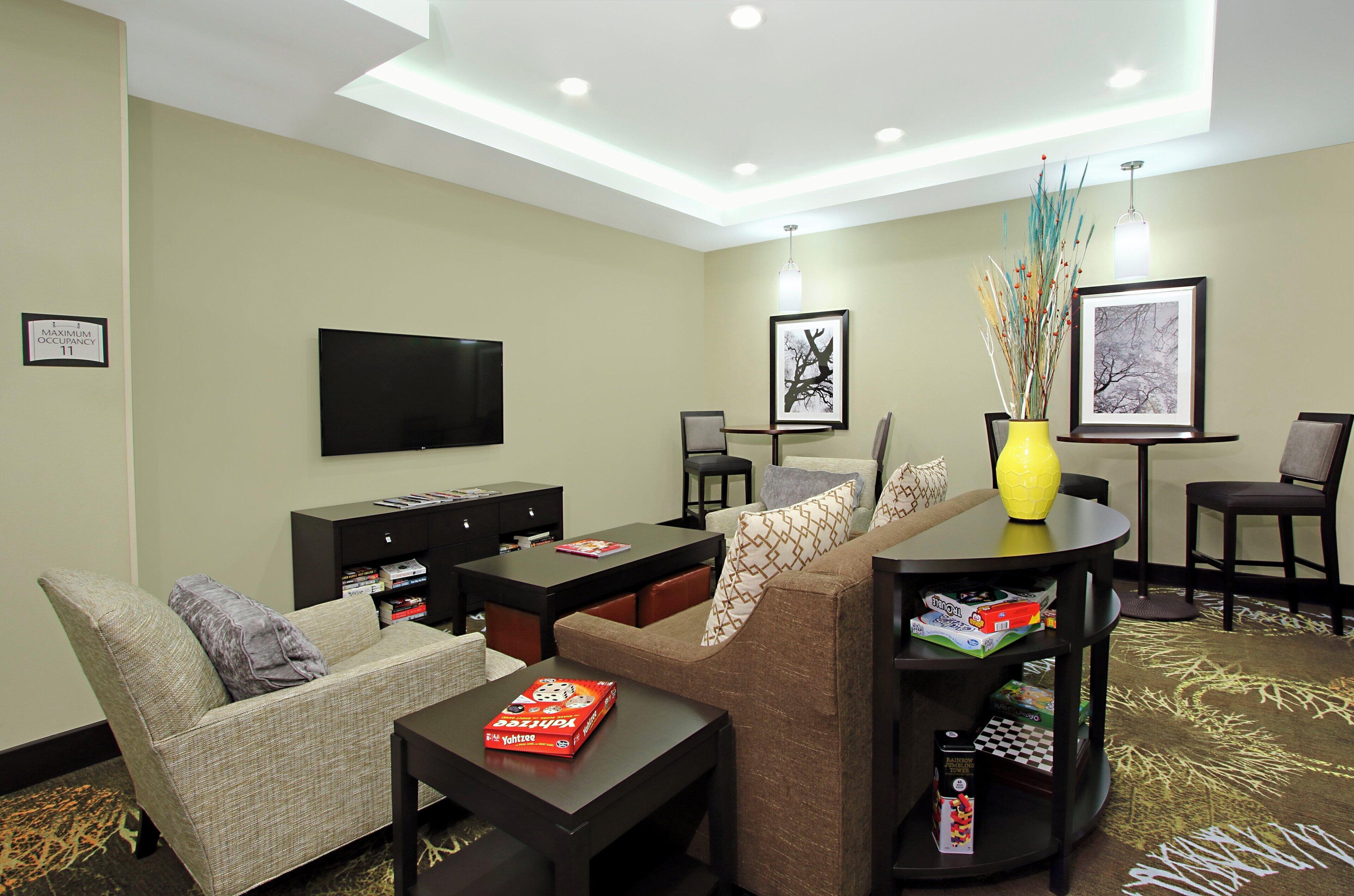 A hotel room with a flat-screen TV, a sofa, a coffee table, and a small dining table with board games.