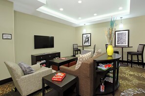 A hotel room with a flat-screen TV, a sofa, a coffee table, and a small dining table with board games. - Staybridge Suites Houston - Medical Center by IHG (Houston)