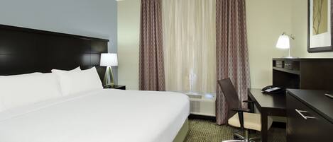 A hotel room with a large bed, a desk, a chair, a lamp, and a framed picture on the wall.