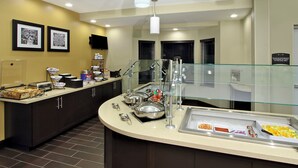 A hotel breakfast area with a buffet setup, including various food containers and a glass railing. - Staybridge Suites Houston - Medical Center by IHG (Houston)