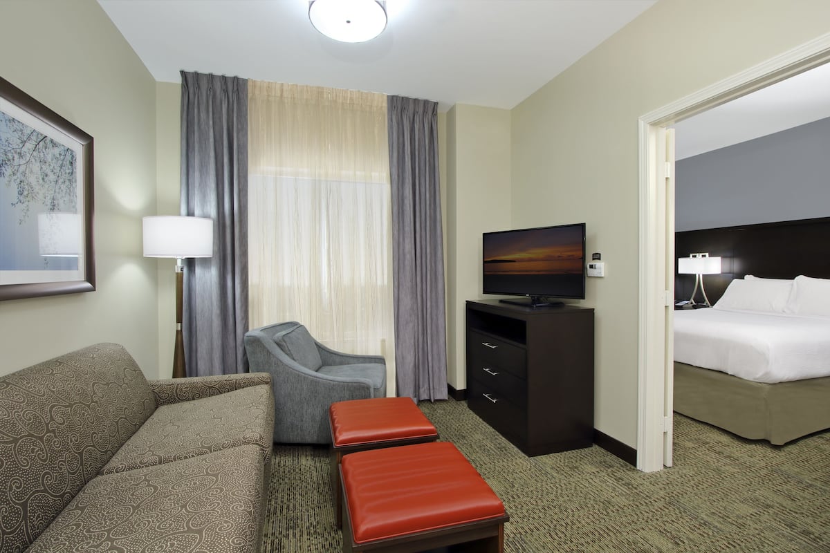 A hotel room with a sofa, a chair, a TV, a dresser, and a bed.