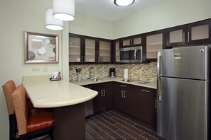 A modern kitchen with dark wooden cabinets, stainless steel appliances, a marble countertop, and a built-in bar area with cushioned seating. - Staybridge Suites Houston - Medical Center by IHG (Houston)
