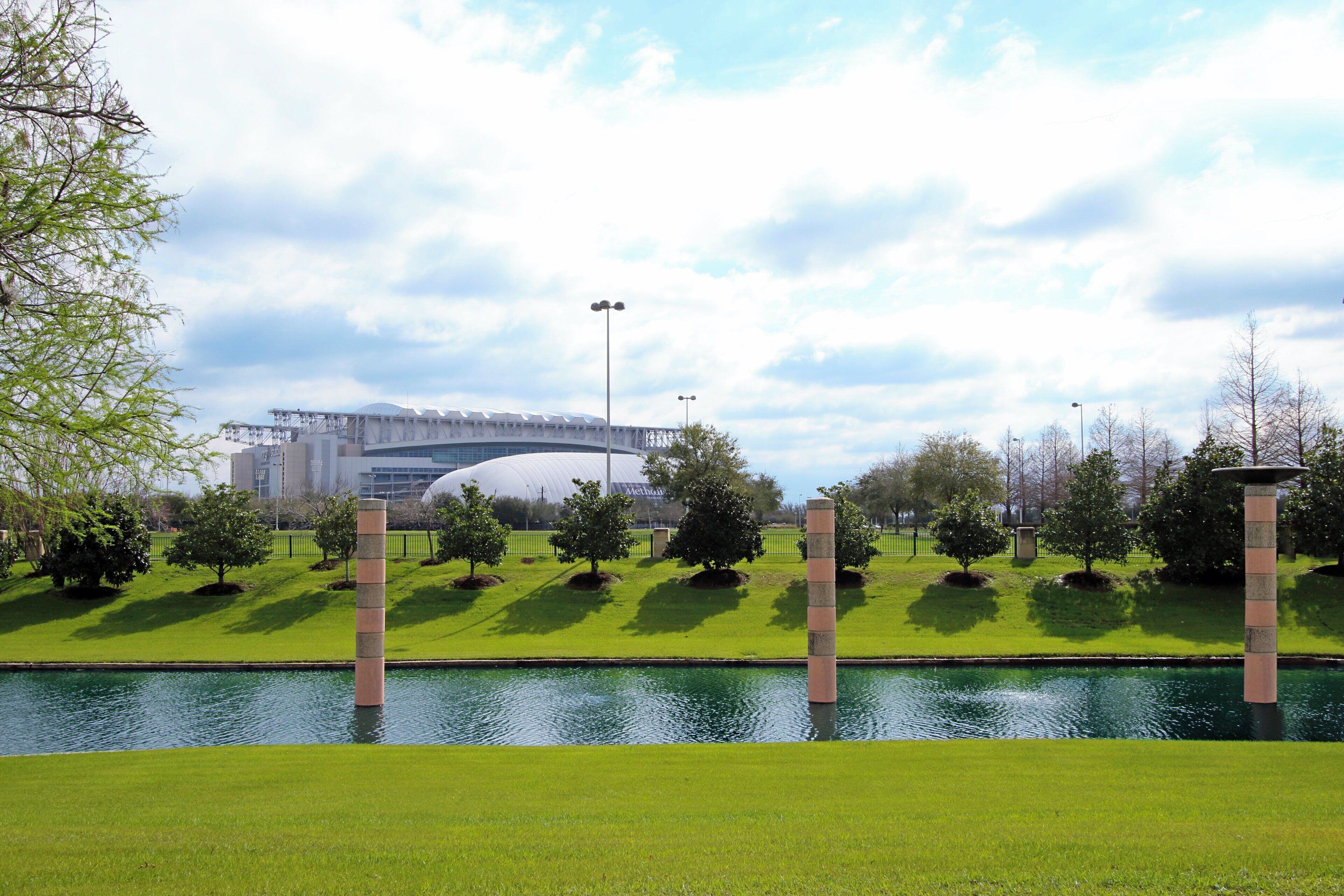 Un parque con fuente de agua, árboles y un puente al fondo.