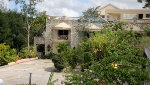 A two-story building with a stone facade, a balcony, and a garden area with various plants and flowers.