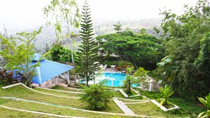 A lush garden with a swimming pool, a blue-roofed structure, and a view of the surrounding hills.