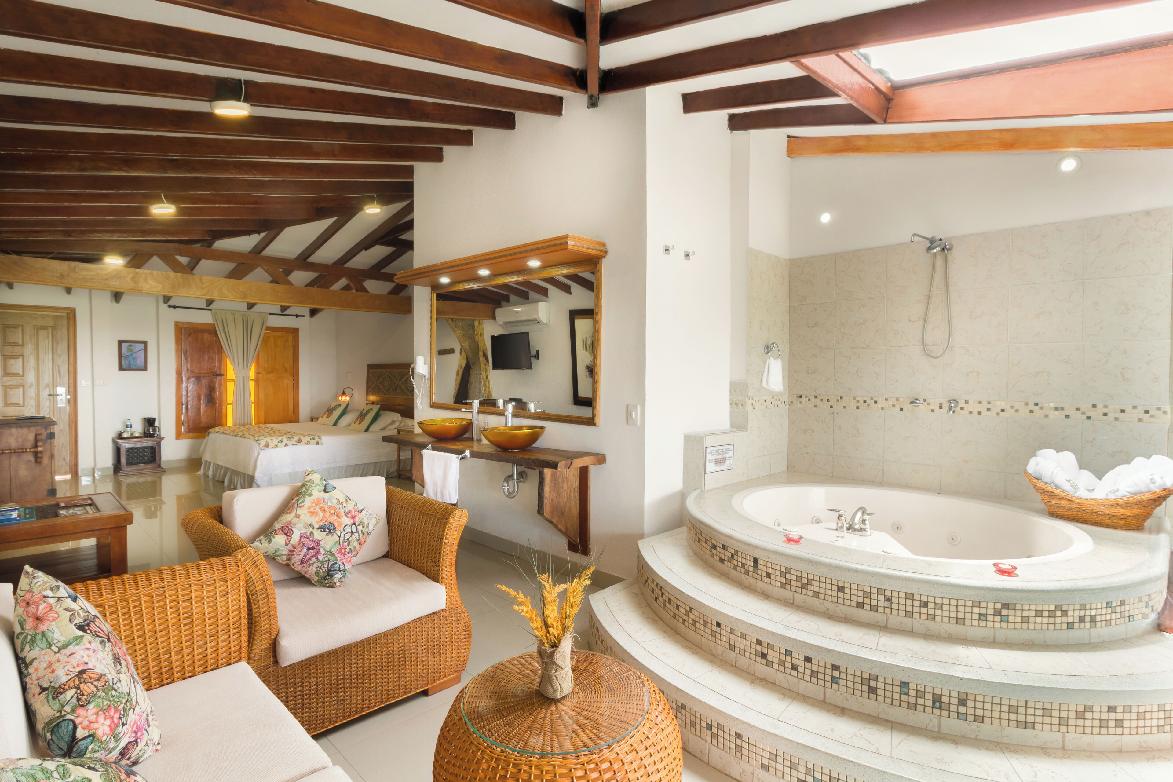 A bathroom with a large bathtub, a sink, and a shower. There is a wicker chair and a wicker ottoman in the room.