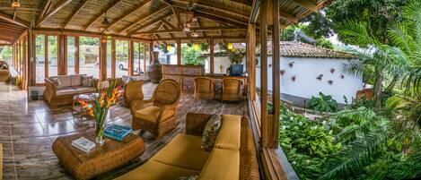 A spacious indoor area with wicker furniture, a large vase with flowers, and a view of lush greenery outside.
