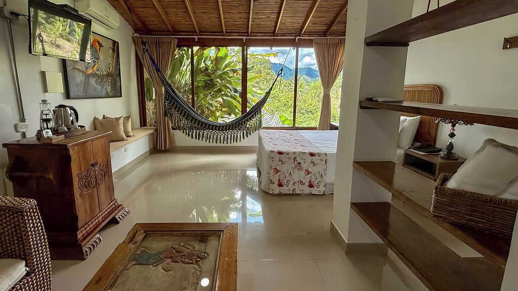 A spacious room with a hammock, a bed with a floral bedspread, a wooden cabinet, and a painting on the floor.