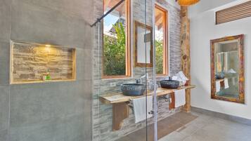 A modern bathroom with a stone wall, a glass shower enclosure, and a wooden vanity with two sinks.