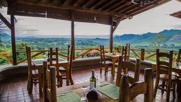Un comedor de madera con una mesa dispuesta para dos, con vistas a un paisaje montañoso.