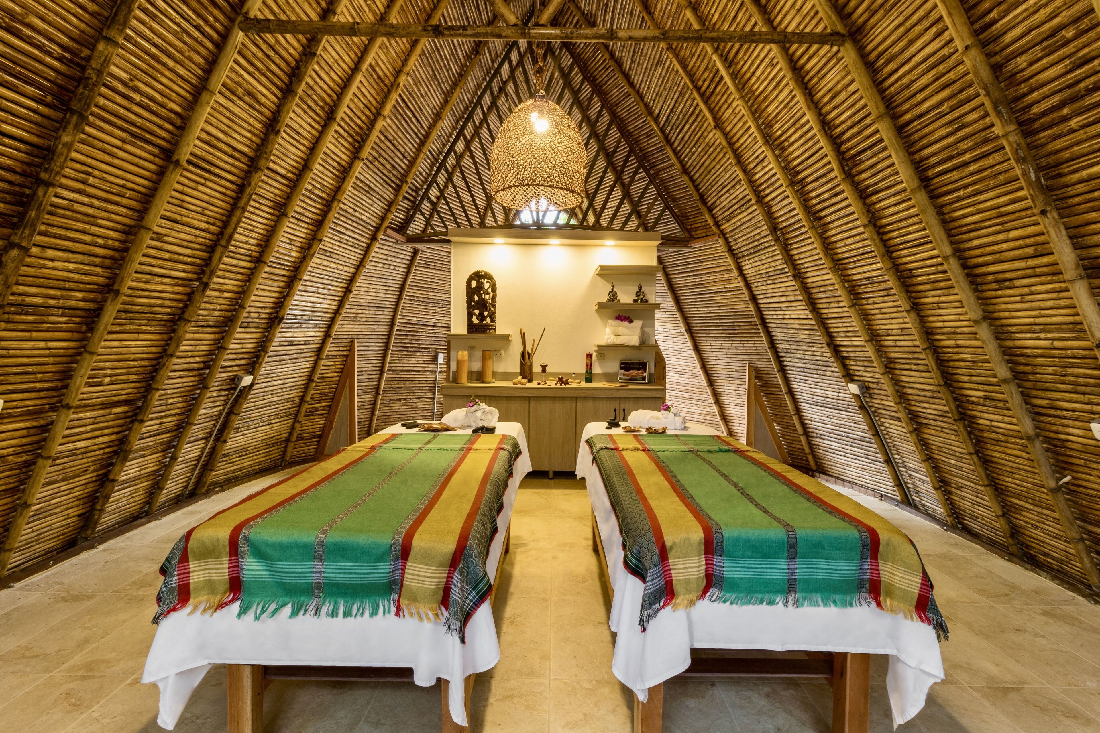 A cozy, thatched-roof room with two beds, a small kitchenette, and a decorative hanging light fixture.