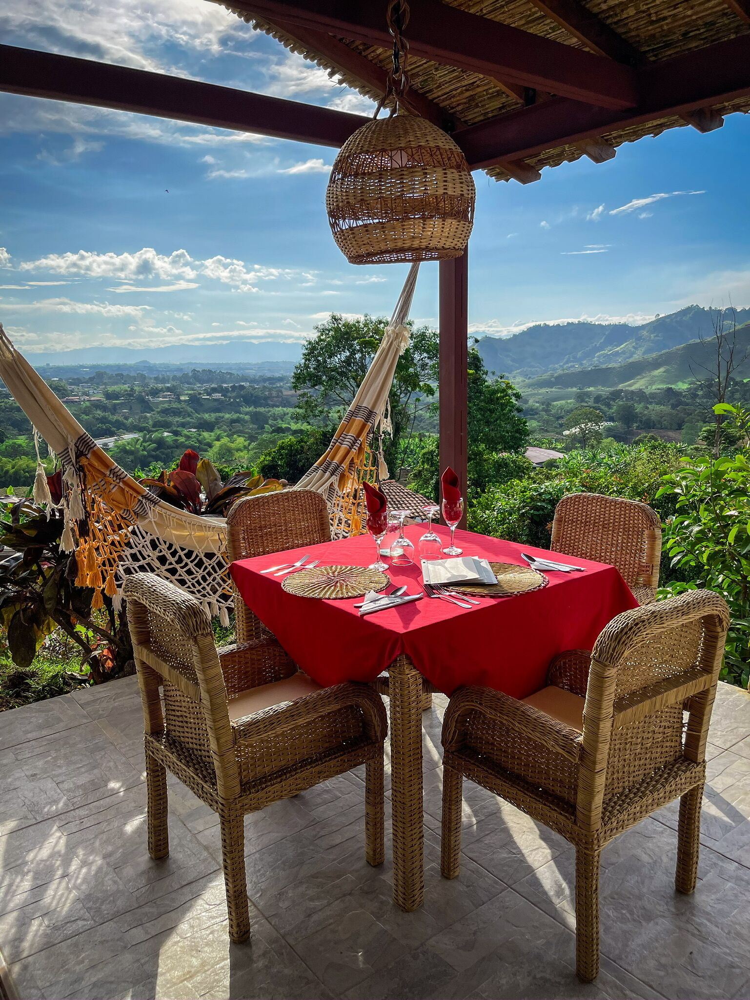 A dining area with wicker furniture and a red tablecloth, overlooking a scenic landscape.
