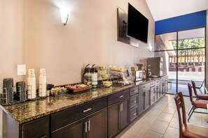 A modern kitchen area with a granite countertop, stainless steel appliances, and a flat-screen TV mounted on the wall.