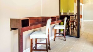 A dining area with a wooden bench and chairs, a glass partition, and a kitchen visible through the partition. - Quality Inn Toccoa (Toccoa)