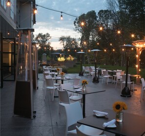 Un patio al aire libre con mesas, sillas, luces colgantes y sombrillas.