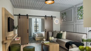 Una sala moderna con sofá, mesa de centro y otomanas. Hay un televisor montado en la pared y una ventana con cortinas.