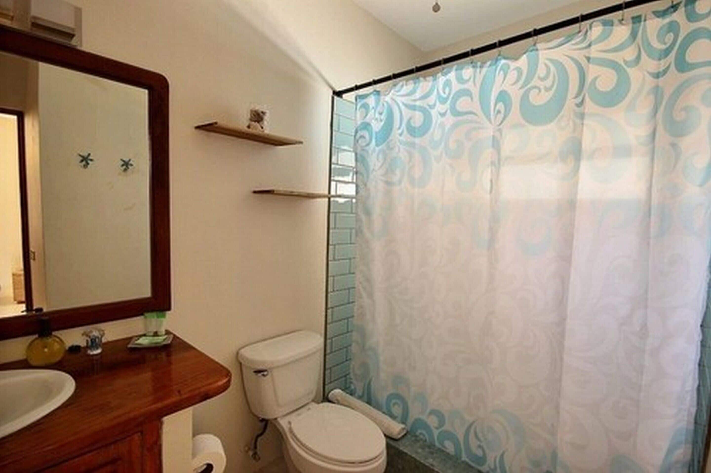 Un baño con tocador de madera, inodoro, cortina de ducha con diseño de remolinos y espejo con marco de madera.