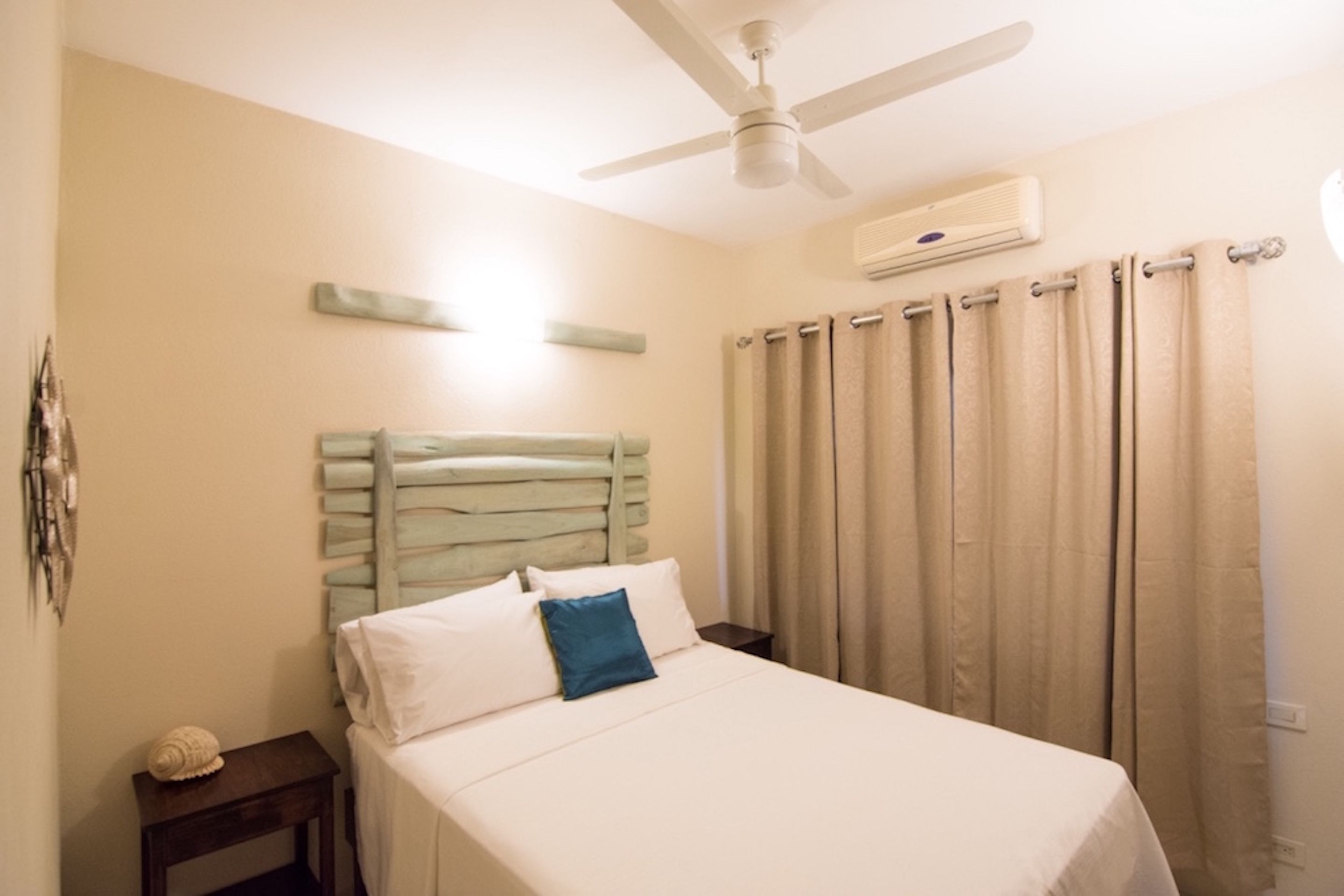 Une chambre à coucher avec un lit, une table de chevet, un ventilateur de plafond et des rideaux beiges.