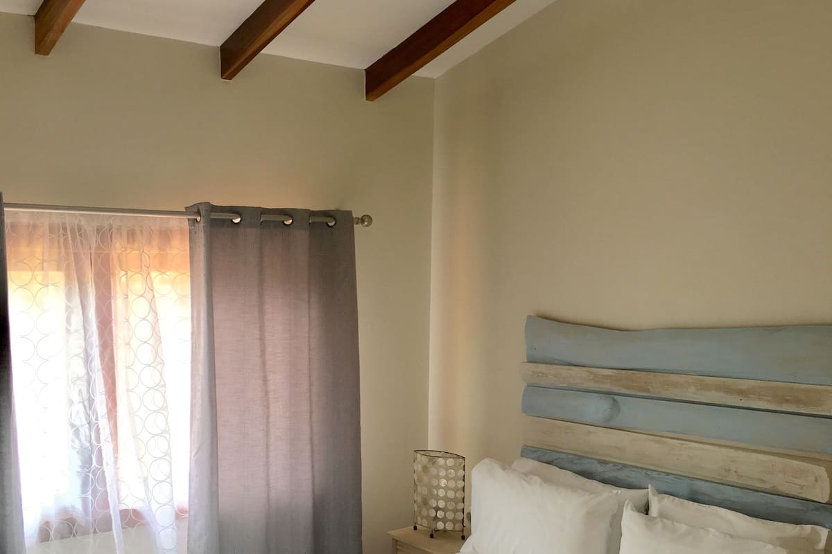 Ein Schlafzimmer mit einem Bett, einem Deckenventilator, einem Nachttisch und einem Fenster mit Vorhängen.
