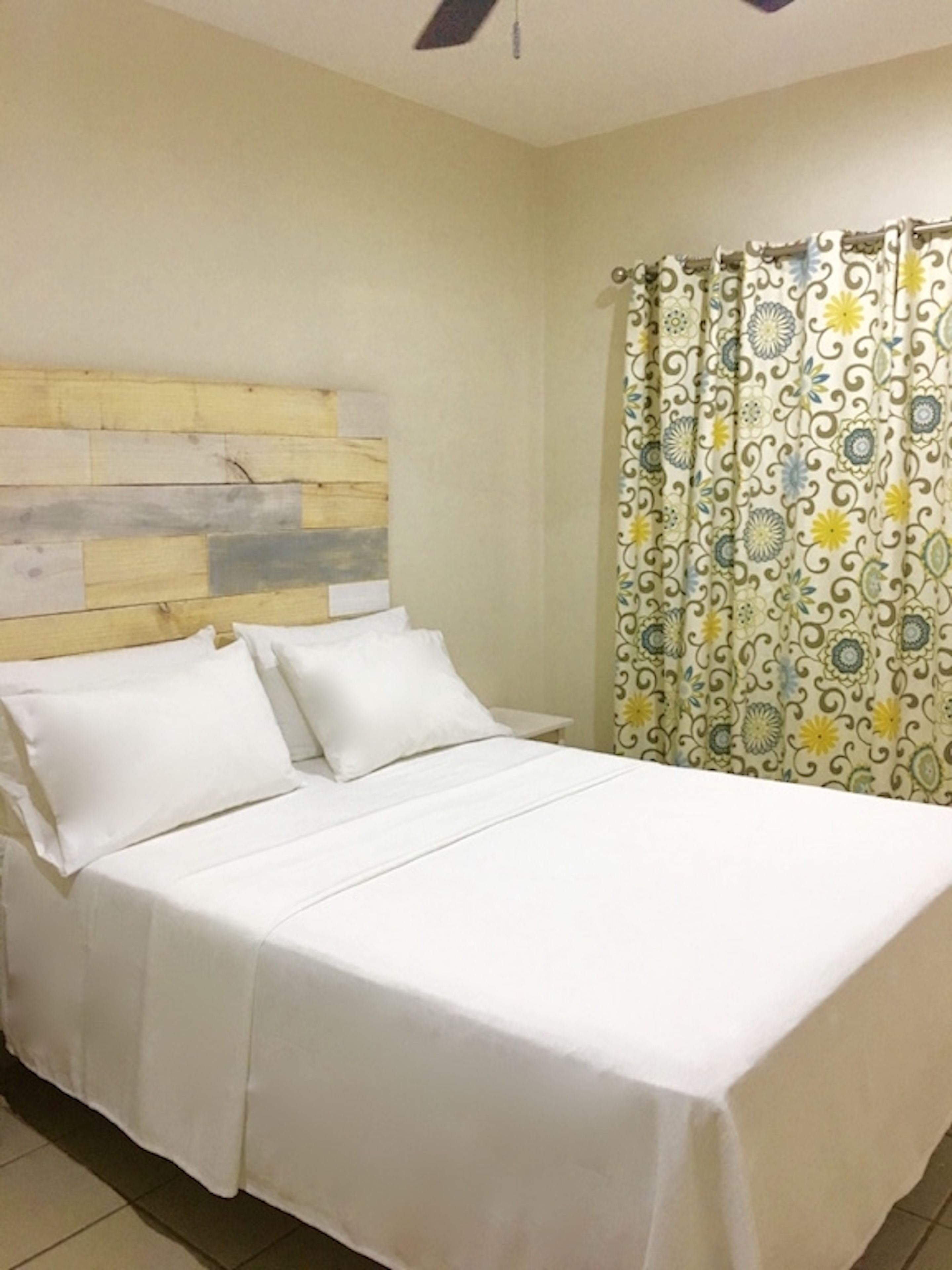 A bed with white bedding, a wooden headboard, and a patterned curtain.