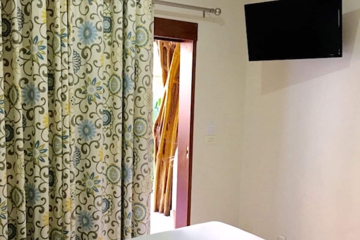 Ein Zimmer mit einem Bett, einem an der Wand befestigten Fernseher und einem Vorhang mit Blumenmuster.
