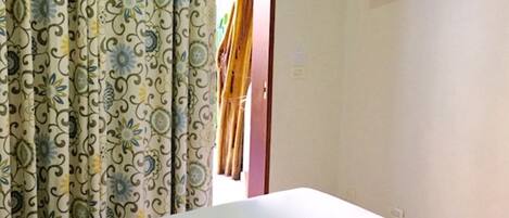 Una habitación con cama, televisor montado en la pared y cortina estampada con motivos florales.