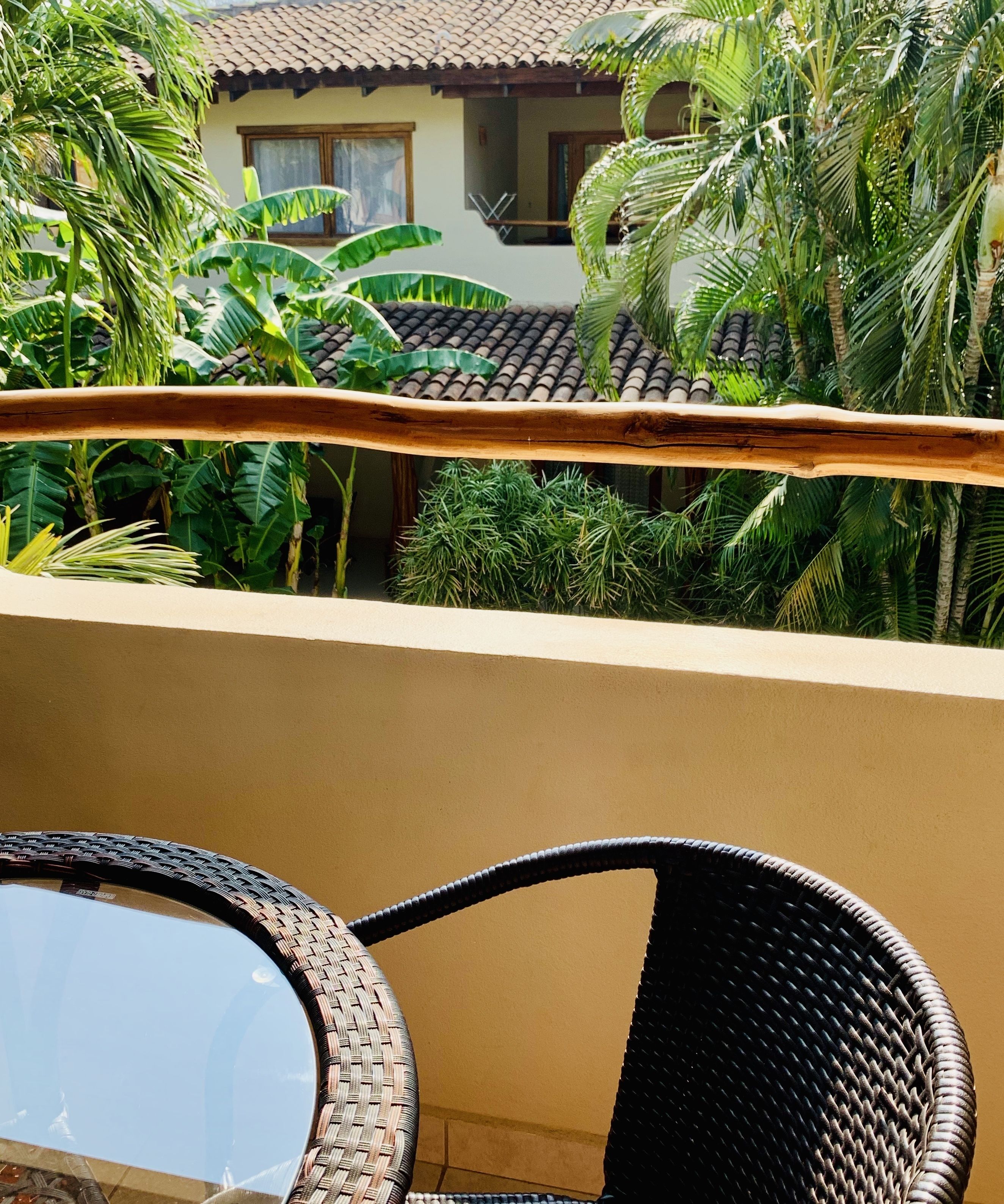 A balcony with wicker furniture and lush tropical plants.