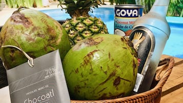 Cestino di vimini con un cocco verde, un ananas, una bottiglia e una lattina di latte di cocco Goya.
