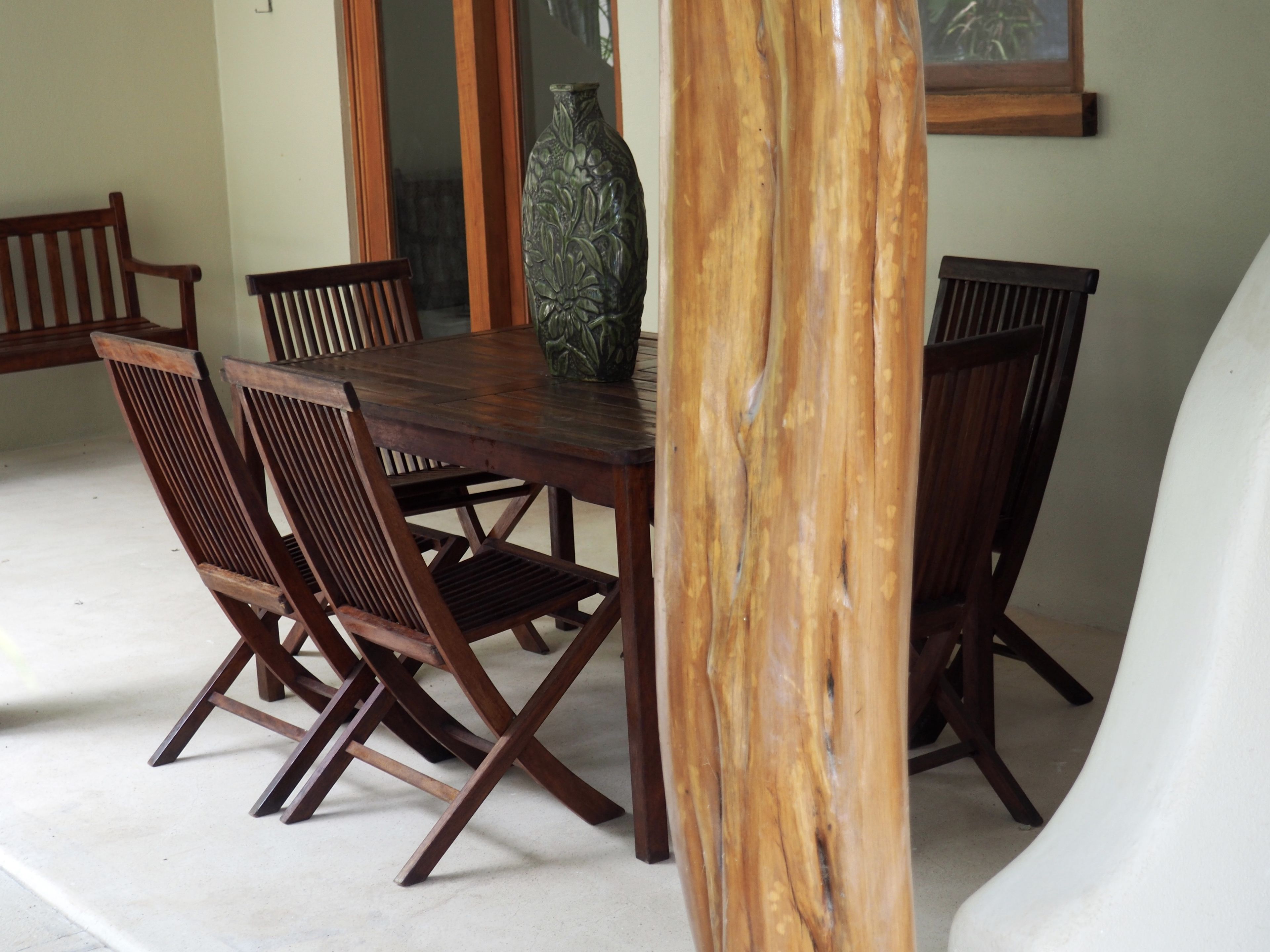 Een houten eettafel met zes stoelen, een vaas en een houten zuil.