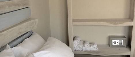 Habitación de hotel con cama, almohadas, estante con toallas y un radio.