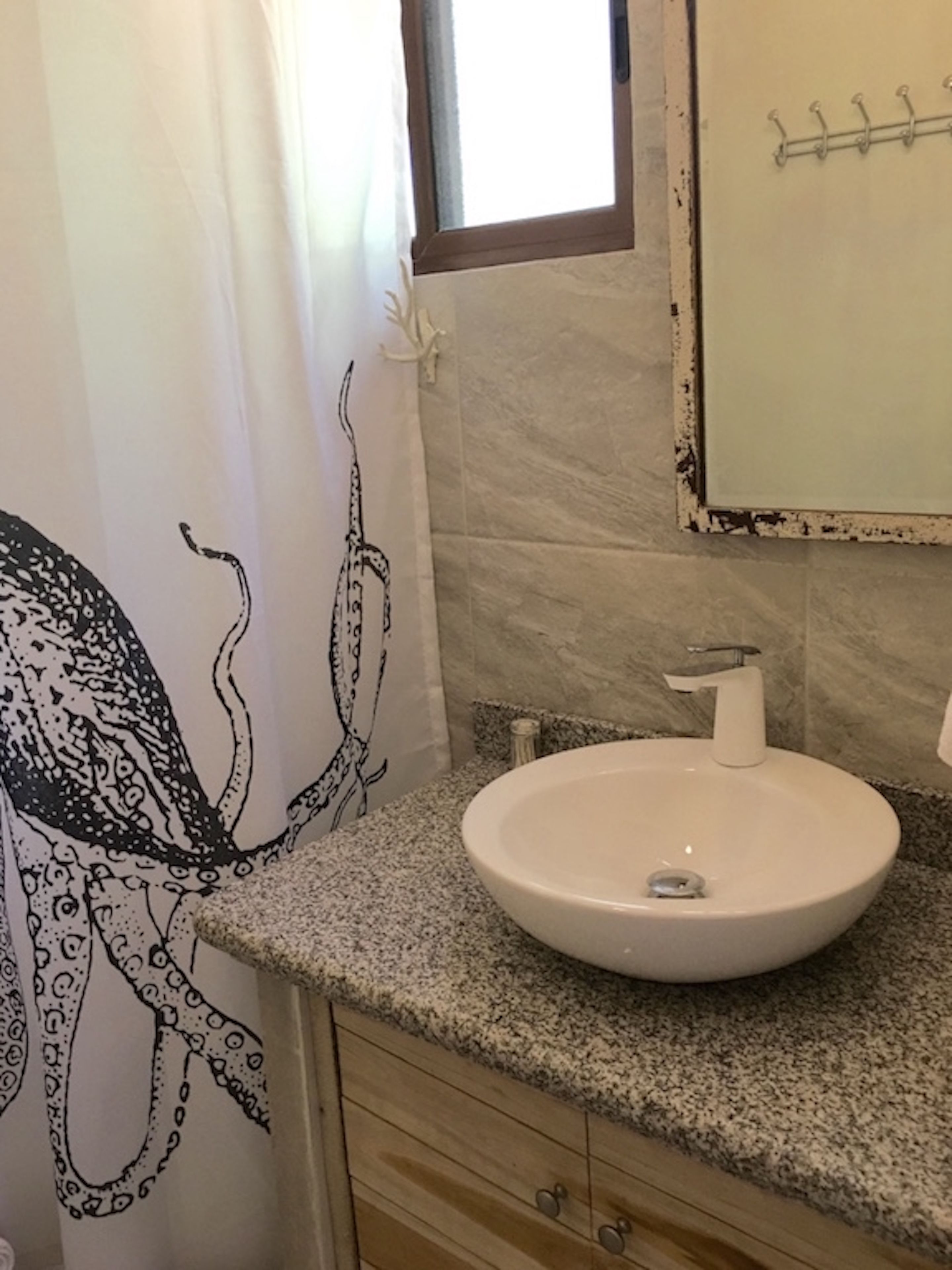 A bathroom with a white sink, wooden cabinets, and a shower curtain featuring an octopus design.