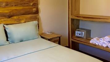 Uma cama com cabeceira de madeira, mesa de cabeceira com rádio e prateleira com toalhas.