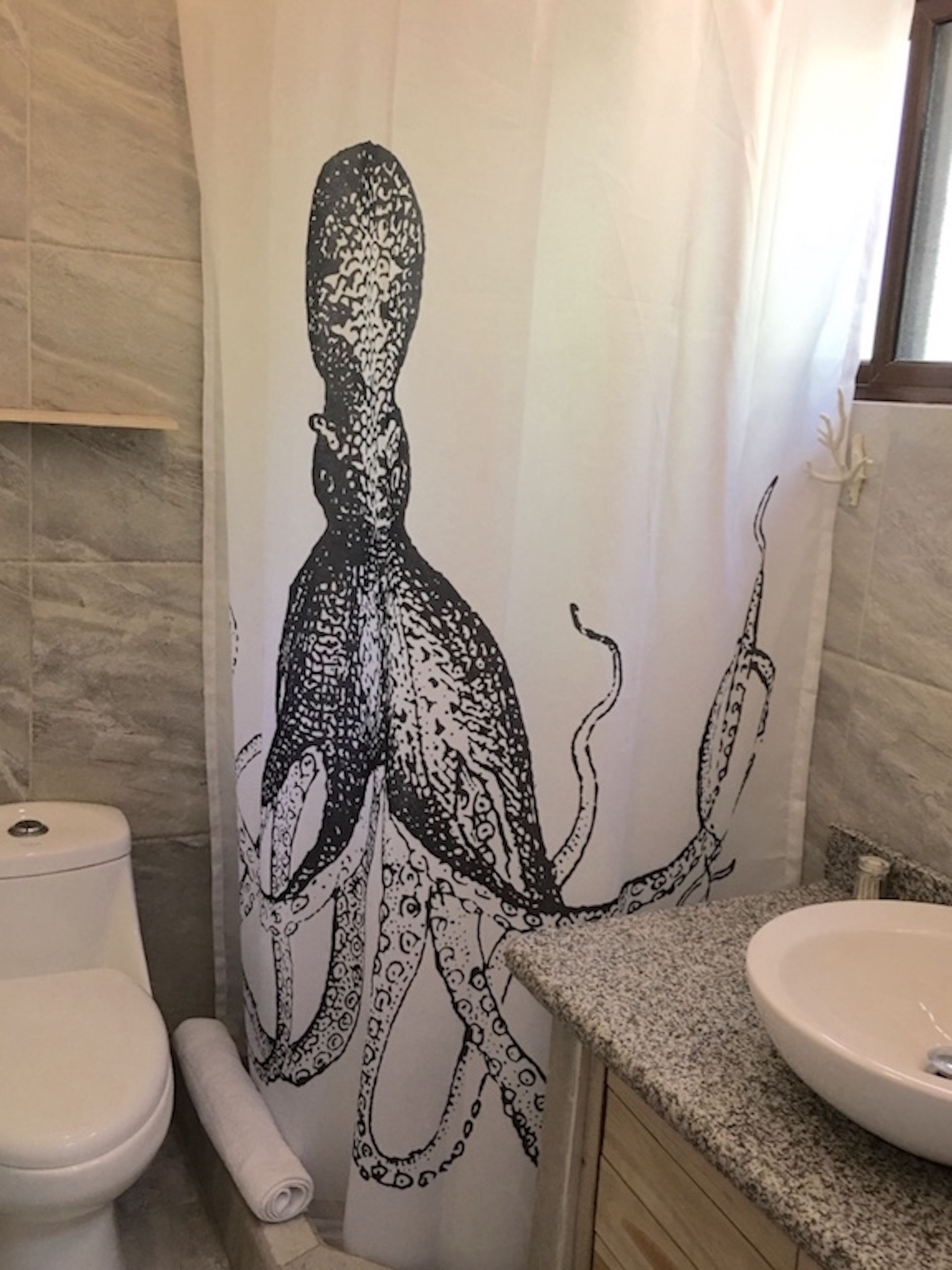 A bathroom with a shower curtain featuring an octopus design, a toilet, and a sink with a granite countertop.
