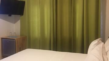 Una habitación con una cama, un televisor de pantalla plana montado en la pared y una mesita de noche de madera con un recipiente de vidrio.
