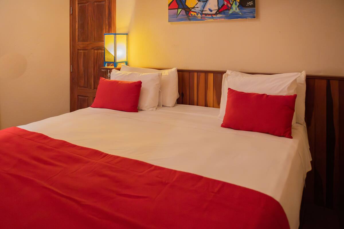 Una cama con una colcha roja y blanca, dos almohadas rojas y un cabecero de madera.