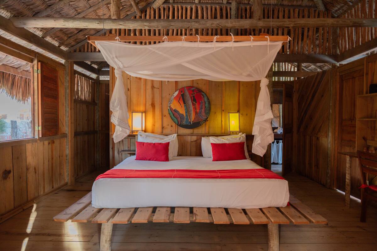 Una habitación de madera con una cama, un banco y un dosel.