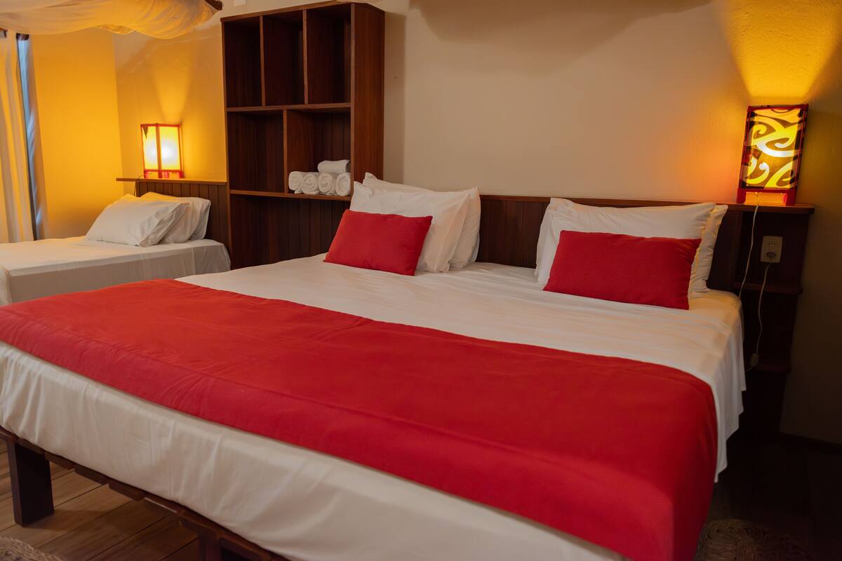 Habitación de hotel con una cama grande, dos mesitas de noche, un estante de madera con toallas y dos lámparas de pared.