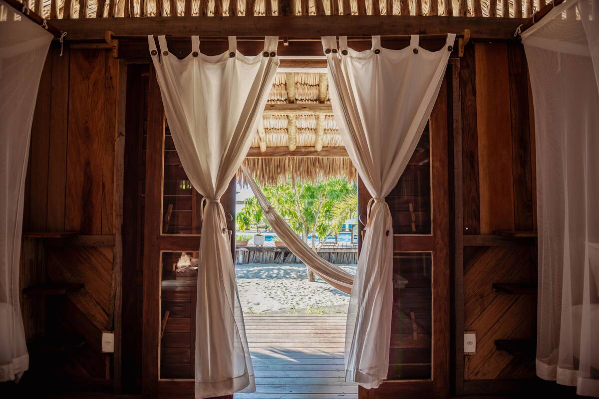 Una puerta de madera con cortinas blancas que dan a vista de playa.