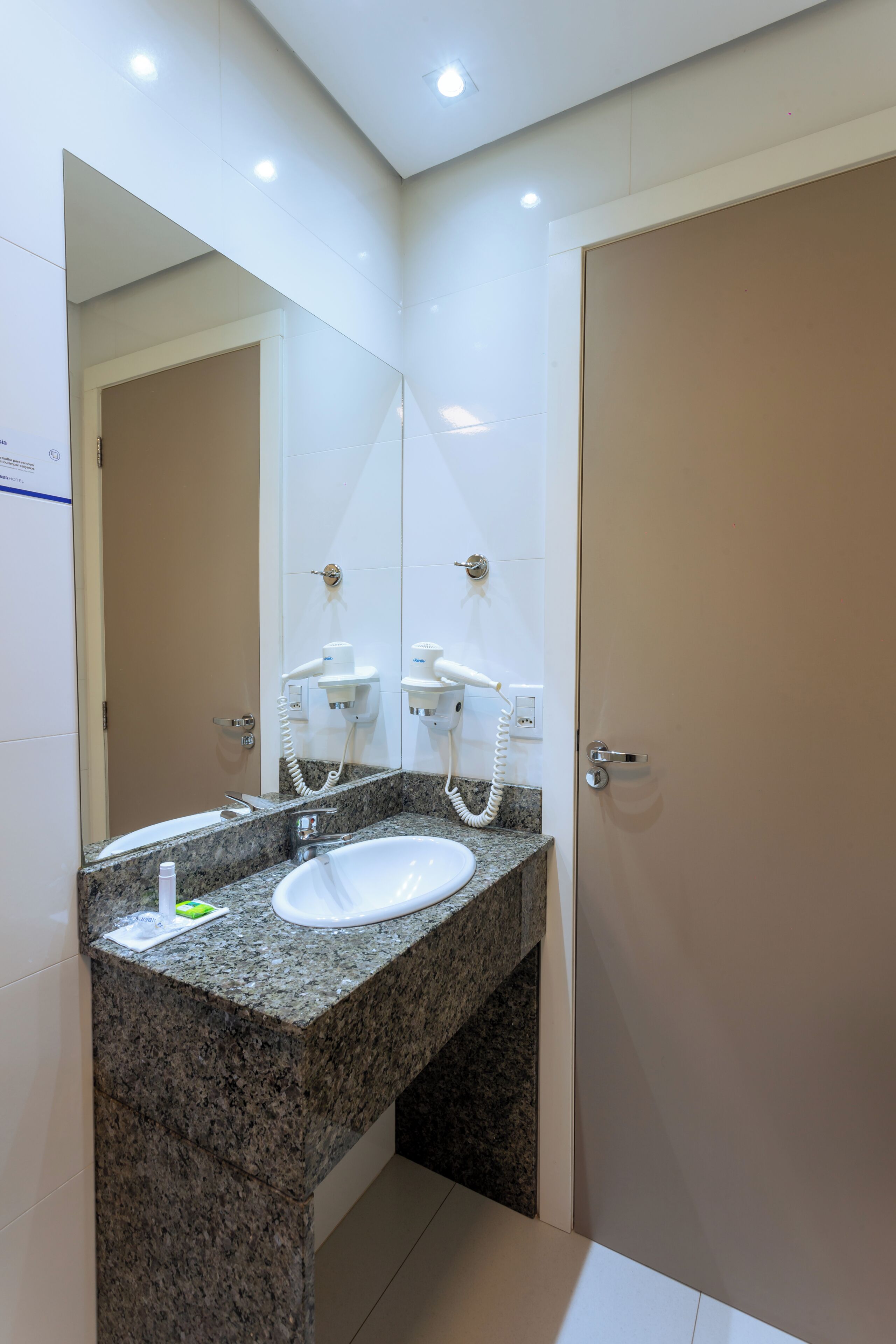 A bathroom with a granite countertop, a white sink, a mirror, and a towel dispenser.