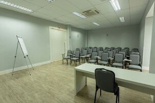 Una sala de conferencias con una mesa larga, varias sillas, un soporte para pizarra blanca y una puerta con la inscripción 'EXIT'.