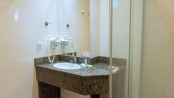 A modern bathroom with a granite countertop sink, a glass shower enclosure, and a large mirror.