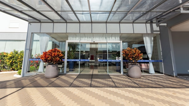 A modern building entrance with a glass door, potted plants, and a tiled floor.