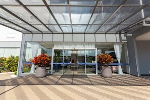 Una entrada de edificio moderna con puerta de vidrio, plantas en macetas y piso de baldosas.