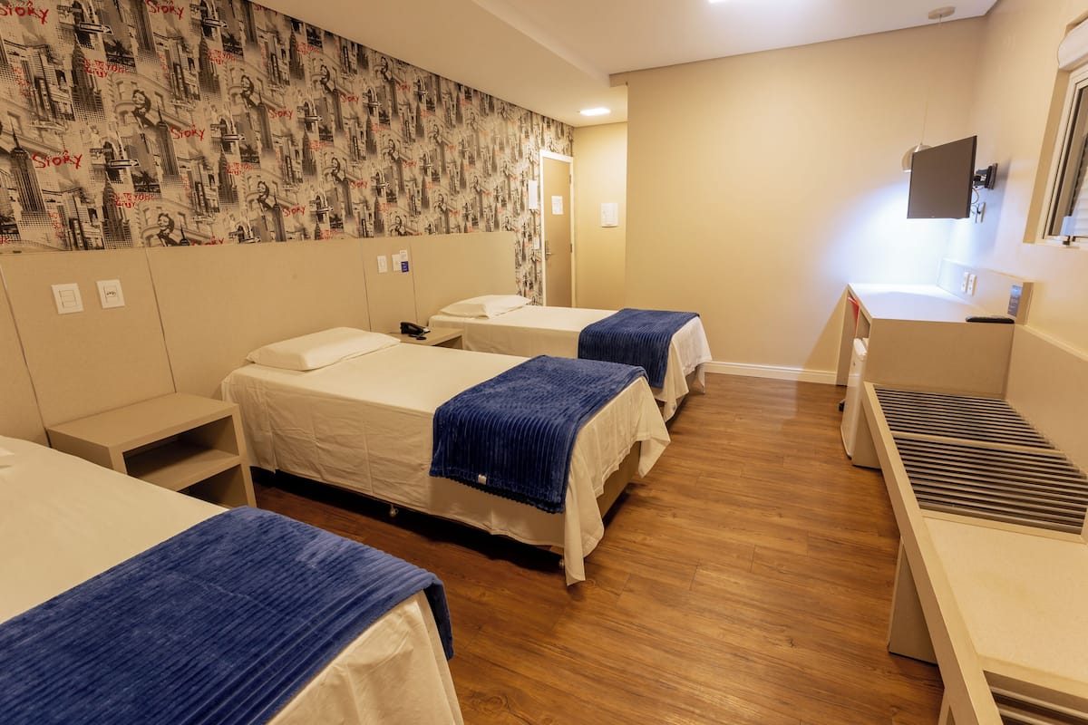Ein Hotelzimmer mit drei Betten, einem Schreibtisch und einem Wandteppich mit Muster.