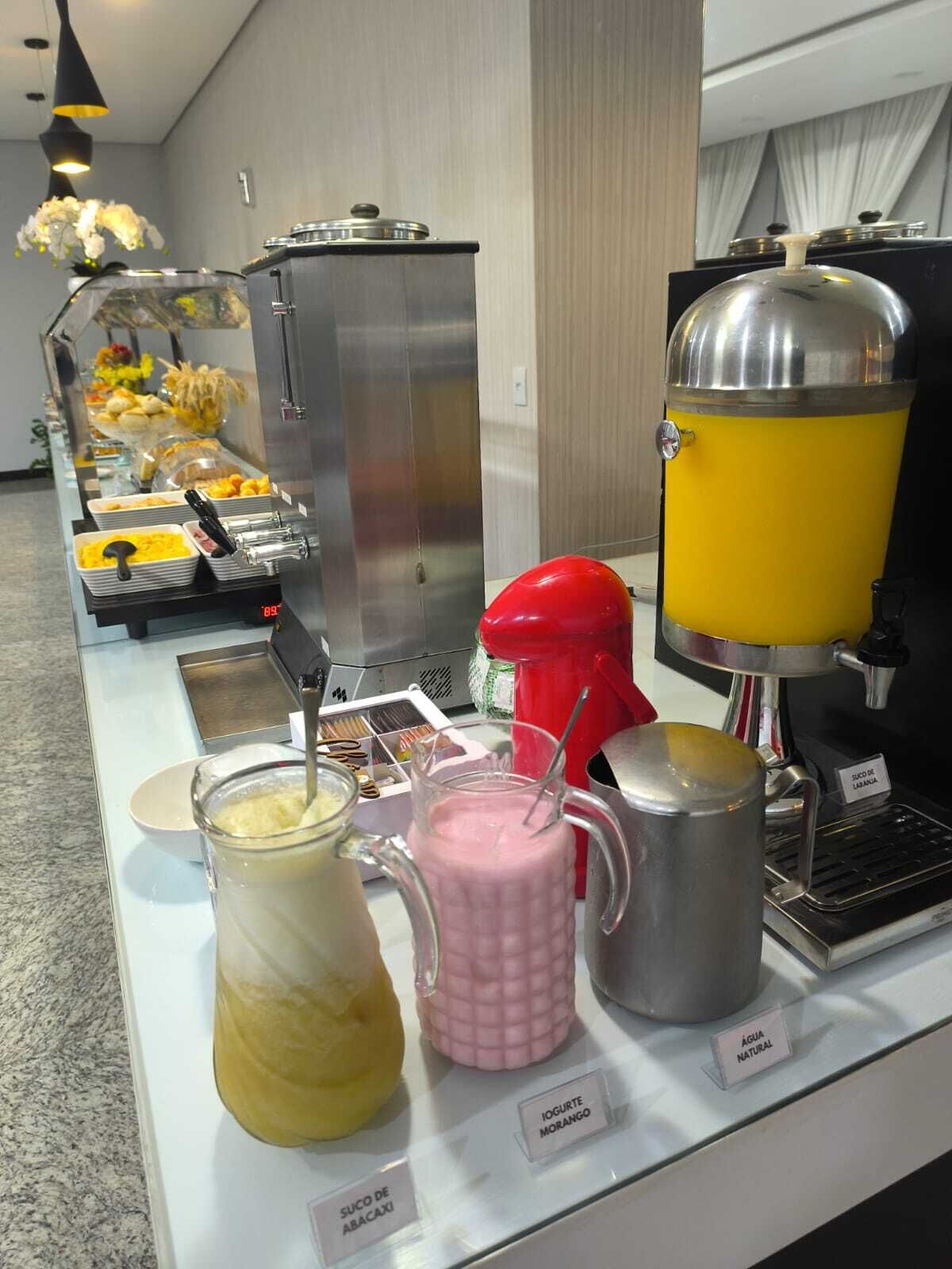 Ein Buffetbereich mit verschiedenen Speisen und Getränken, darunter eine Kaffeemaschine und beschriftete Behälter für unterschiedliche Getränke.