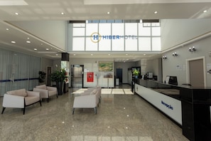 Zona de recepción de hotel con mostrador, asientos y un amplio ventanal.