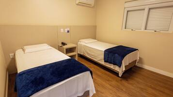 Quarto de hotel com duas camas de solteiro, mesa de cabeceira com telefone, ar condicionado e janela com cortinas.