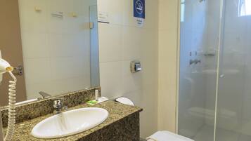 Un baño con encimera de granito, un lavabo blanco, inodoro y ducha con mampara de cristal.