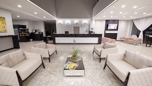 A modern hotel lobby with a reception desk, seating area, and a television.