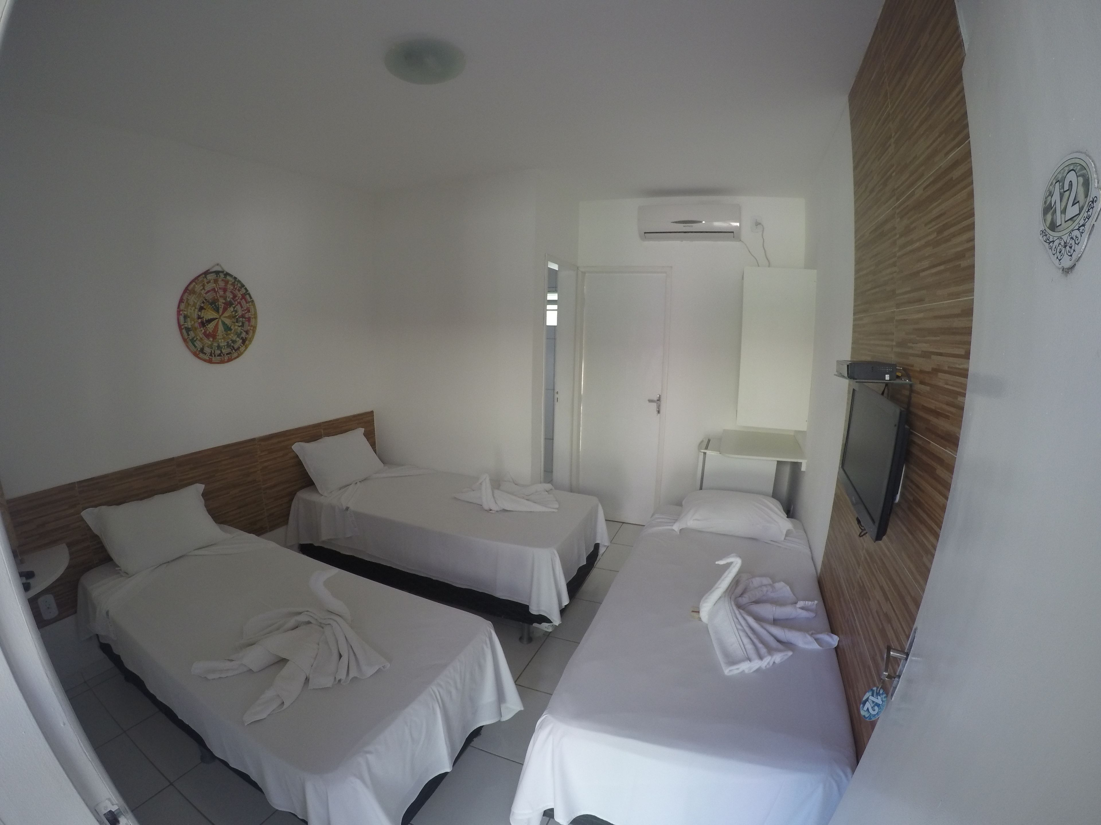 A hotel room with three single beds, a small round table, and a wall-mounted TV.